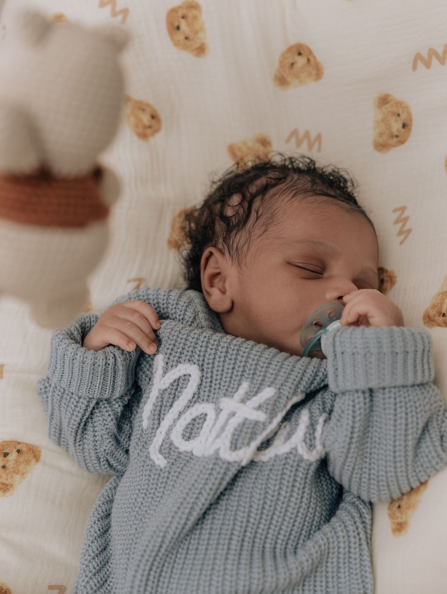 Sleeping baby wearing a cozy gray knit sweater with 'Naps' text against a cookie-patterned background.