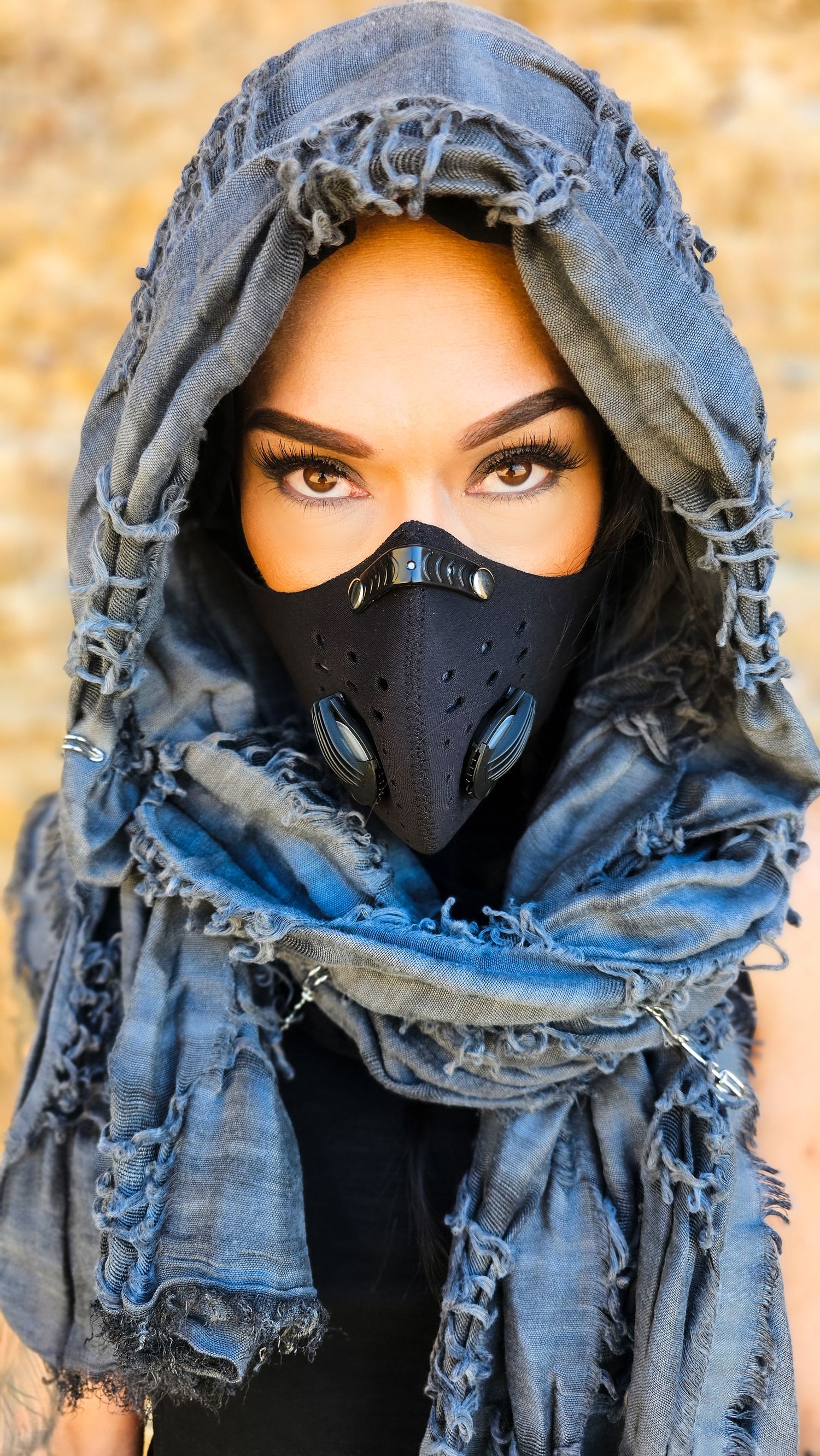Person wearing a black face mask and distressed denim hood gazes intensely at camera in dramatic portrait series.