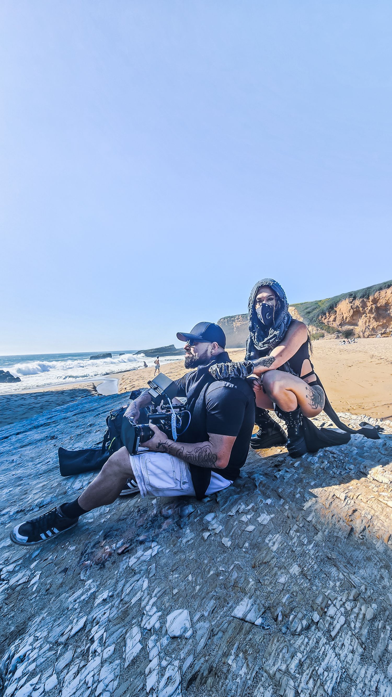 Photographers lying on rocky coastal cliffs while taking pictures of ocean waves during sunset.