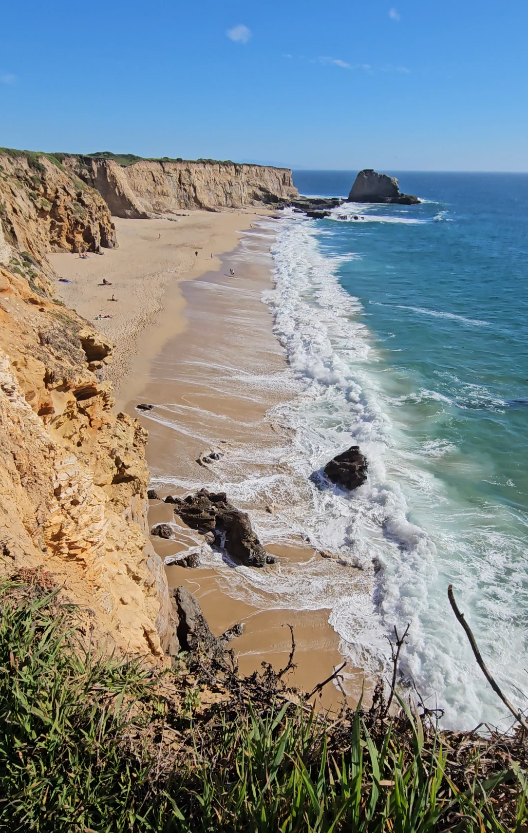 Scenic coastal view of rugged cliffs and sandy beach with crashing waves along the Portuguese coastline under blue skies.