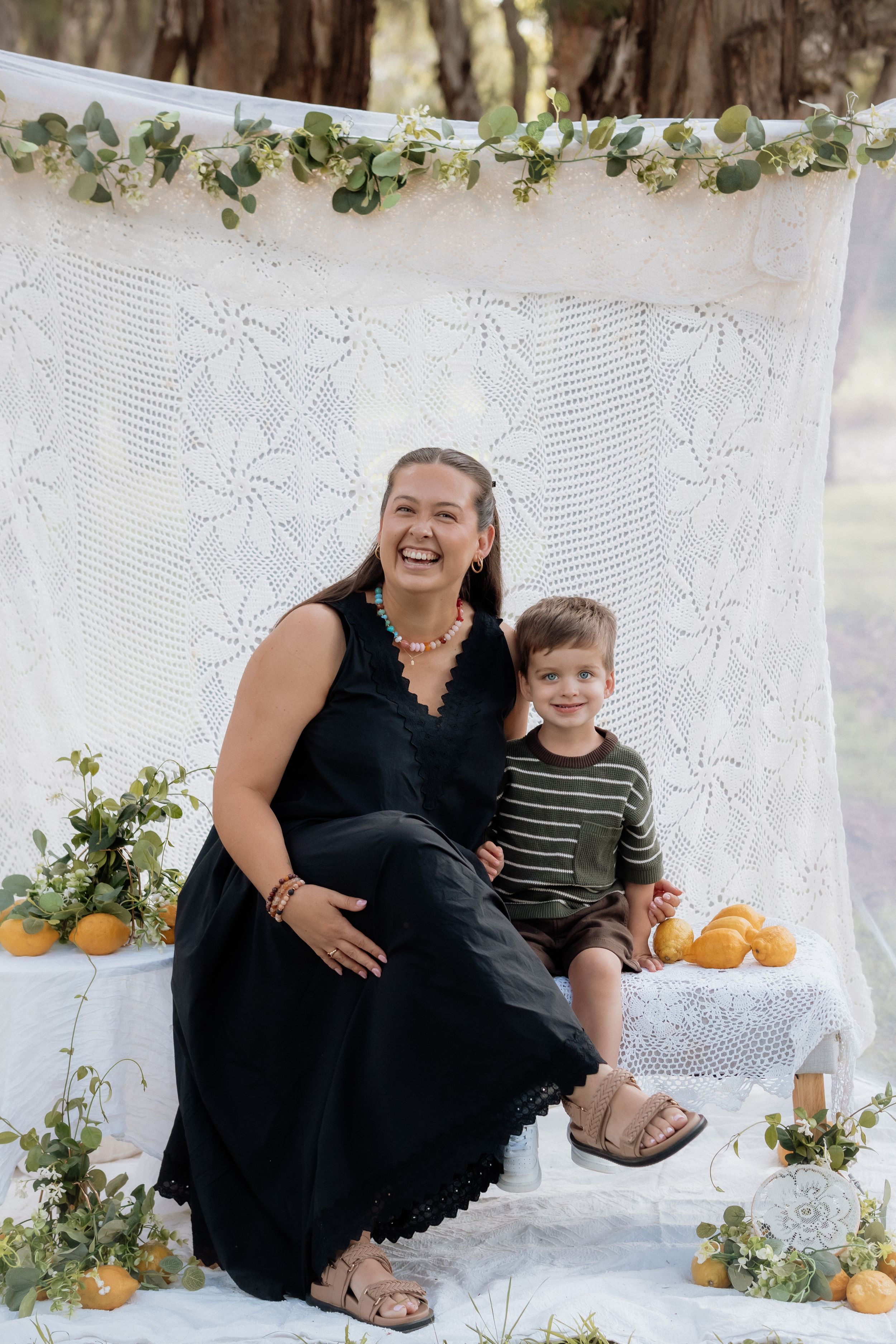 A sweet autumn photo session with pumpkins, white lace backdrop, and greenery decorations creates a cozy setting.
