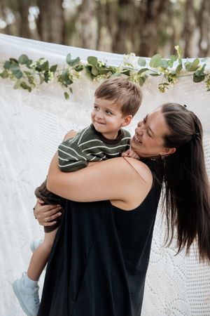 A tender moment captured outdoors with a white backdrop and decorative eucalyptus garland hanging above.