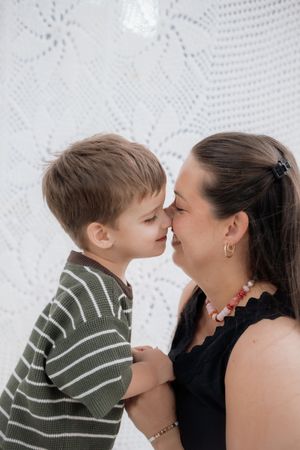 A tender moment between parent and child sharing an intimate nose-to-nose touch against a white lace backdrop.