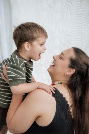 A joyful moment captured showing playful interaction and laughter against a white lace curtain background.