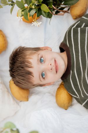Child lying on white lace backdrop with lemons and greenery, wearing striped shirt.