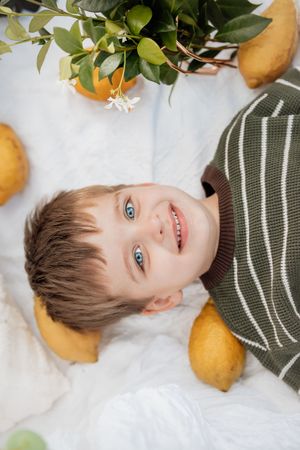 Artistic portrait with citrus fruits and greenery featuring bright blue eyes and a striped sweater.