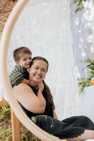 A joyful outdoor portrait captured through a circular frame with white lace and greenery details.