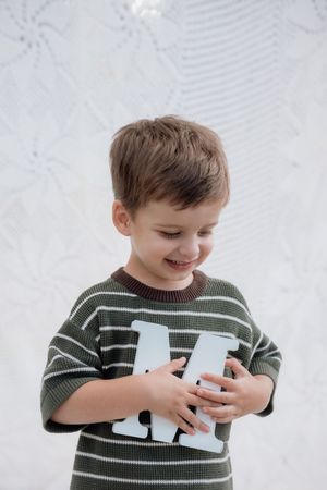 A young child in a green striped sweater smiles while holding and looking at playing cards.