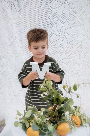 Child in striped sweater plays with decorative elements on white lace backdrop.