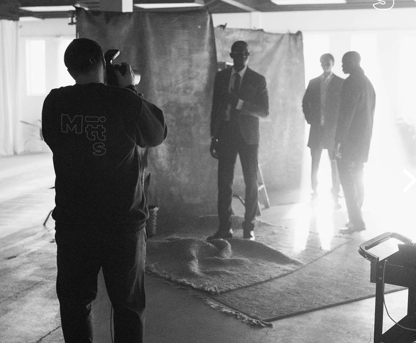 Black and white photo of a photographer shooting a man in a suit against a backdrop in a studio setting.