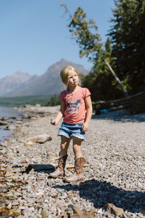 Child playing on rocky beach with mountains visible in background.