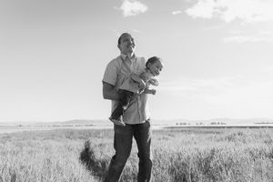 People walking through tall grass field under bright blue sky.