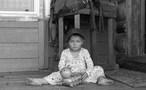 A small dog rests on a wooden porch near a doorway.