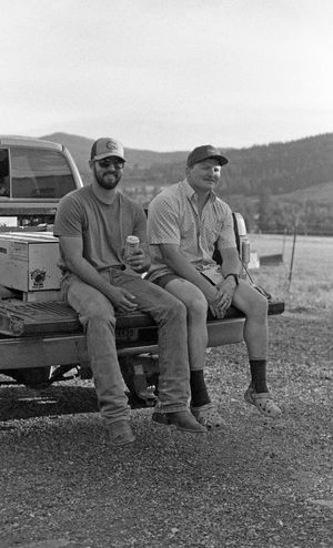 Workers sitting on the tailgate of pickup trucks in a rural mountain setting.