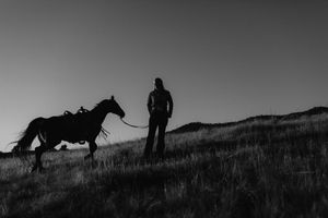 Silhouettes of horses and riders against a dramatic mountain landscape at dusk.