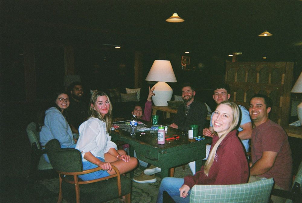 A dimly lit bar or restaurant interior with patrons seated at tables and booths in a casual dining atmosphere.