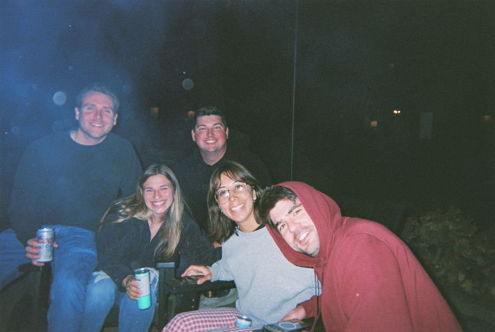 Group of friends enjoying drinks and socializing outdoors at night in a casual gathering.