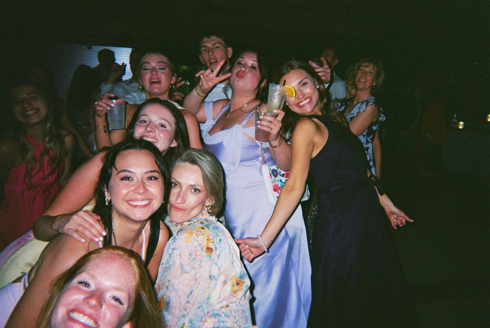 Group of friends celebrating and having fun at a party with flash photography in dimly lit setting.