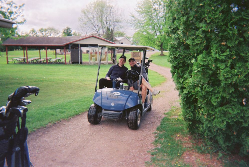 Golf carts drive along a winding path through a lush green golf course on a sunny day.