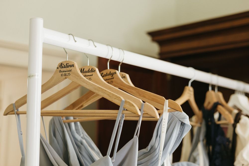 Wedding attire hangs neatly on wooden hangers against a rustic wall with peeling paint.