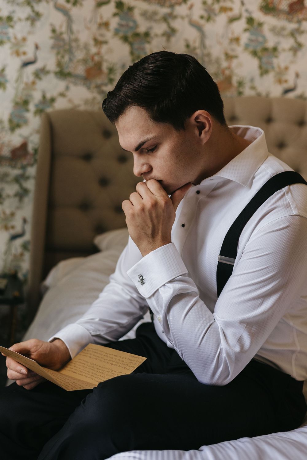 A person in a white dress shirt and black vest reads an emotional letter while sitting.