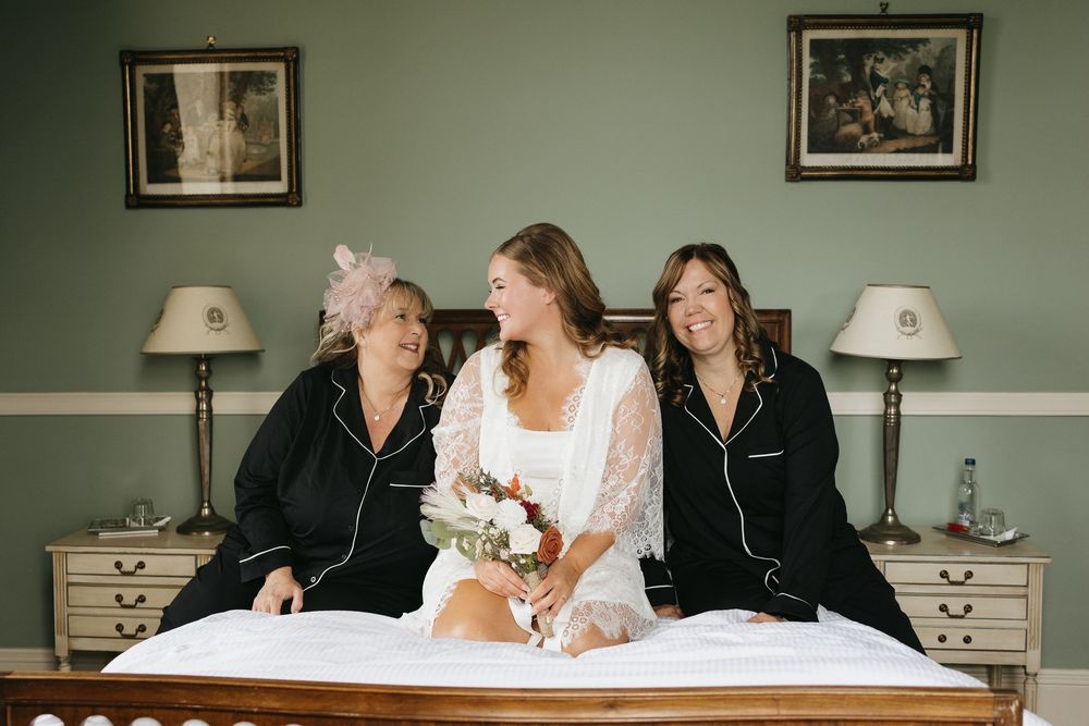 Wedding party members relax on a bed in coordinated outfits before the ceremony.