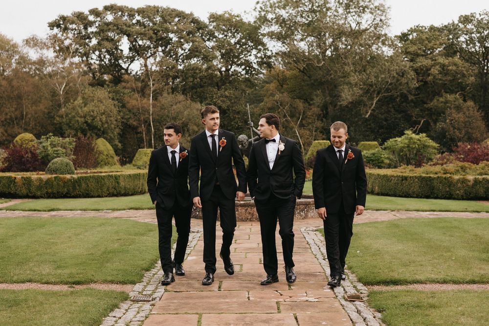 Wedding party walking along a stone path surrounded by autumn trees and landscaped gardens.