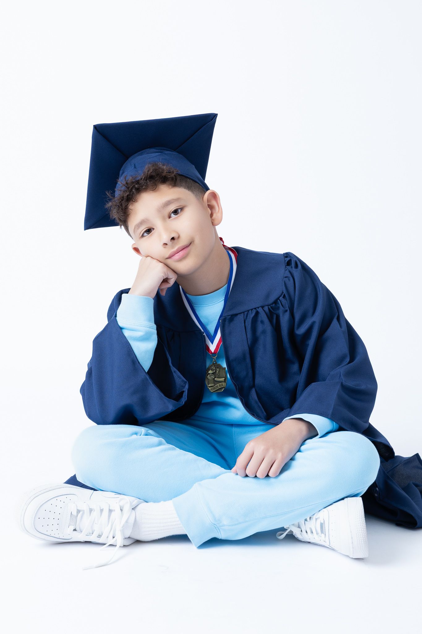 Graduate in blue cap and gown poses playfully on white background.
