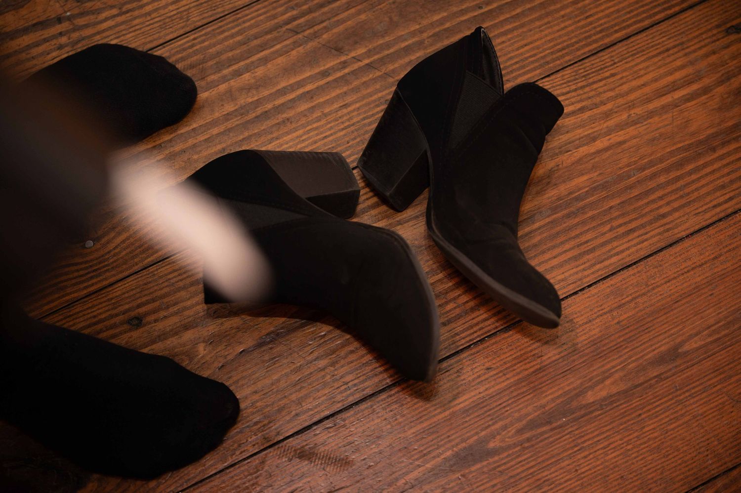 Black boots cast shadows on a wooden floor in dramatic lighting.