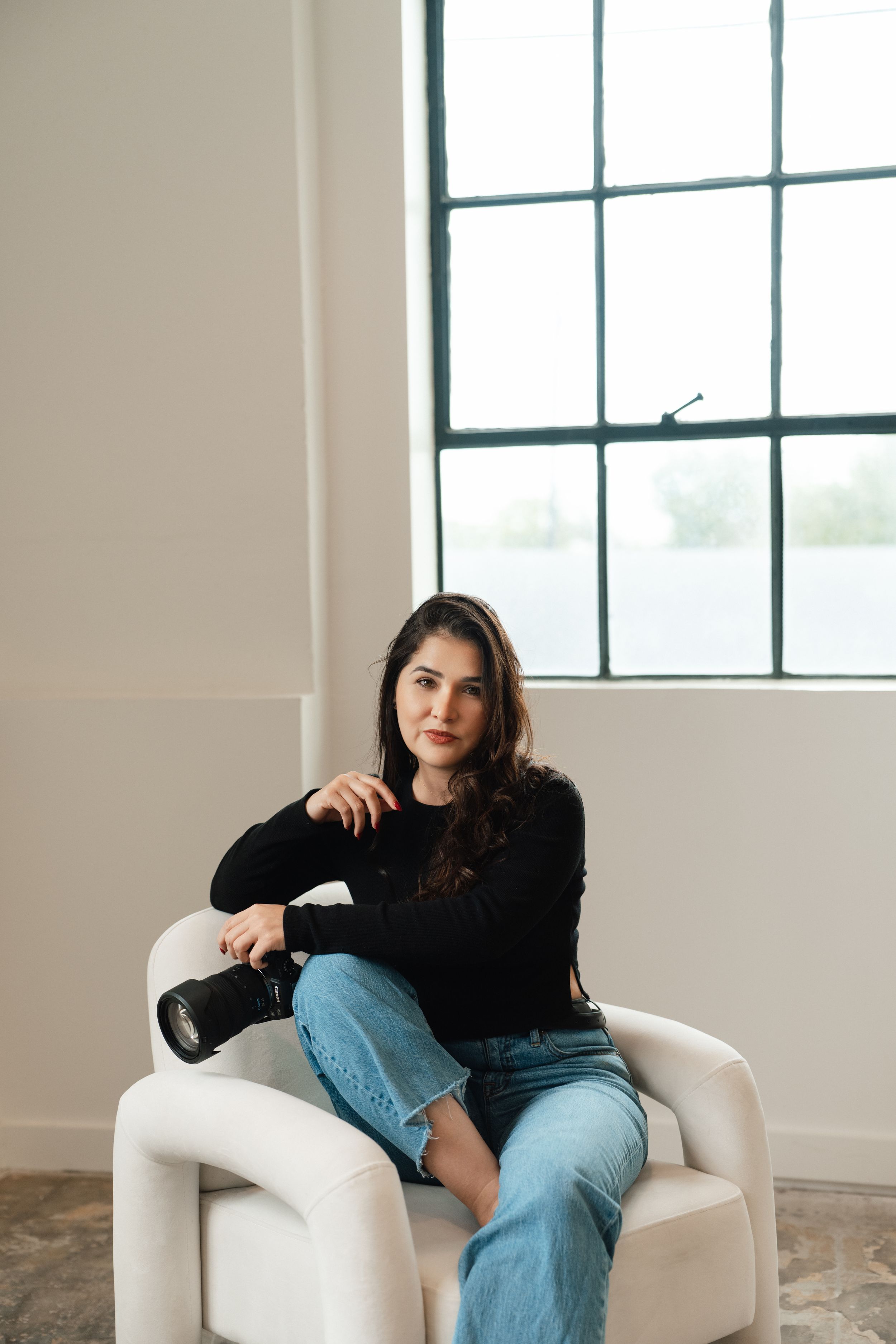 Photographer sitting with camera equipment and laptop on white background.