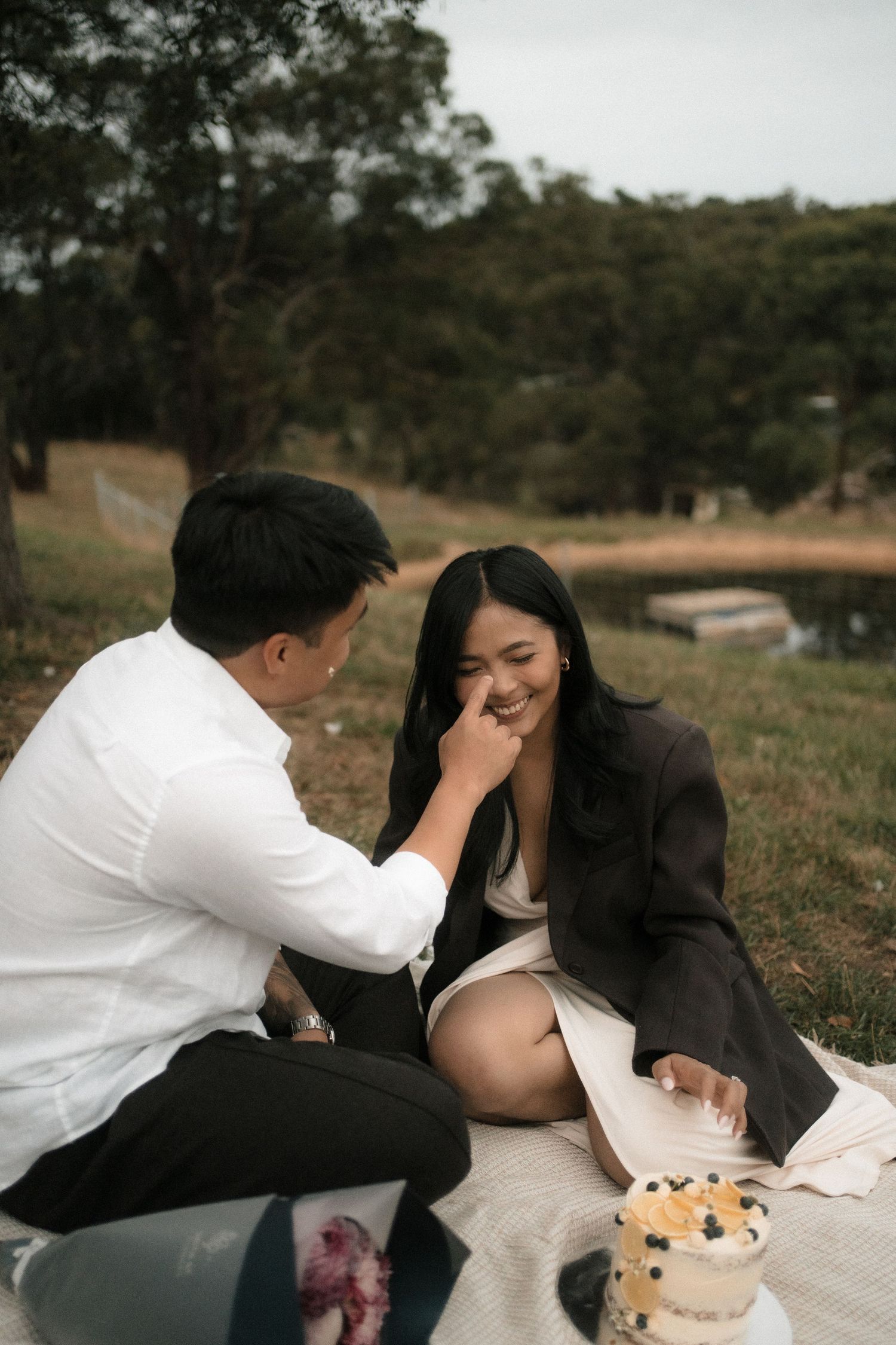 A romantic couple shares tender moments on a picnic blanket in a grassy field during an outdoor photoshoot.