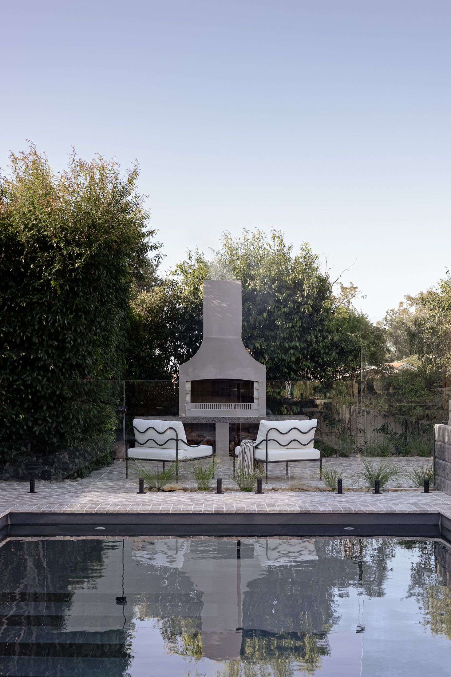 Modern outdoor pool with geometric concrete features and decorative wave patterns reflects trees and sky in still water.