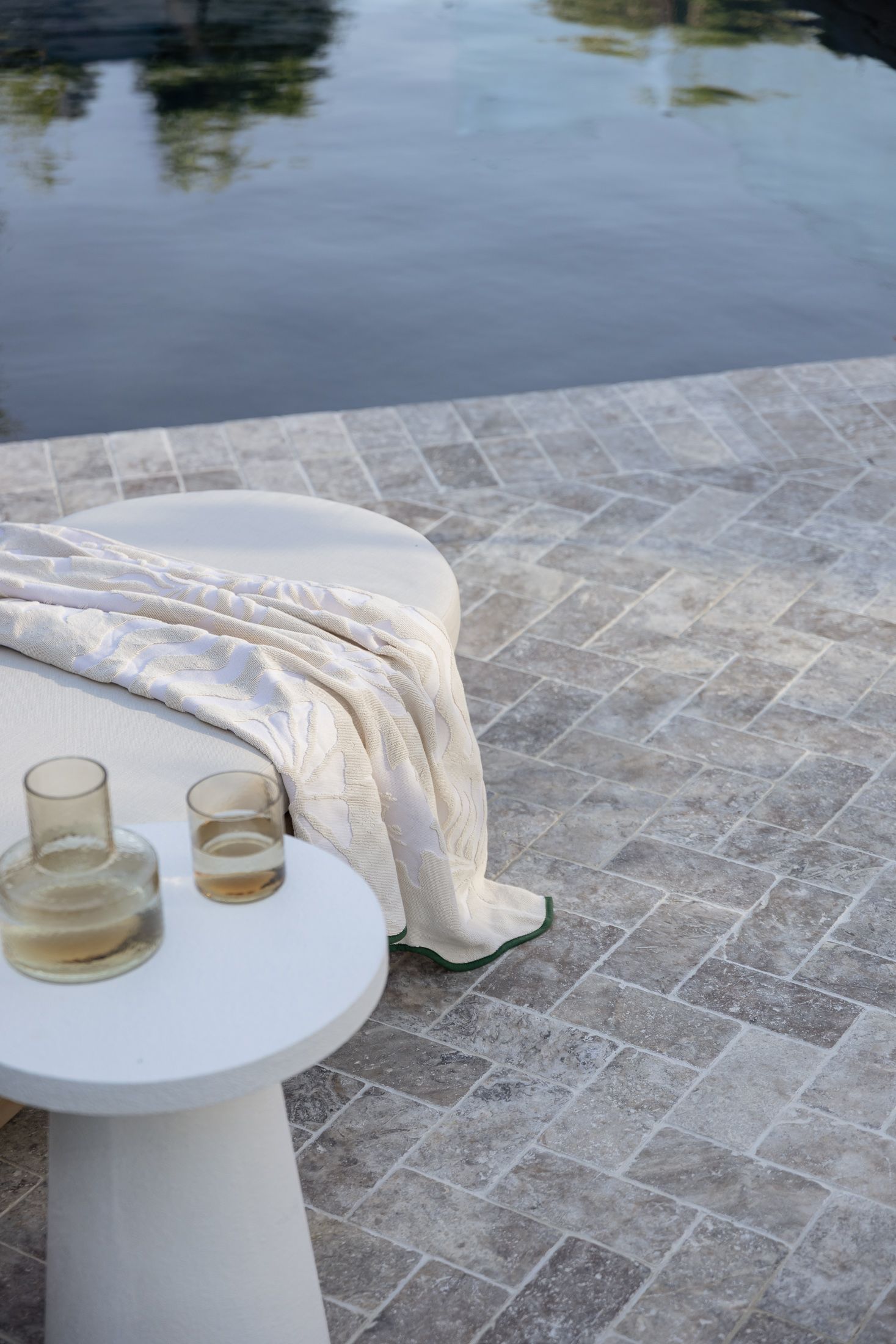 Two amber-tinted glass cups sit on a white round pedestal table against a stone paver patio background.