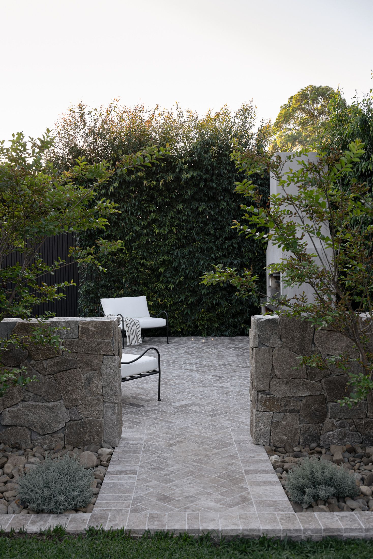 Stone wall pillars line a curved garden path with paving stones and landscaped greenery in a tranquil outdoor setting.