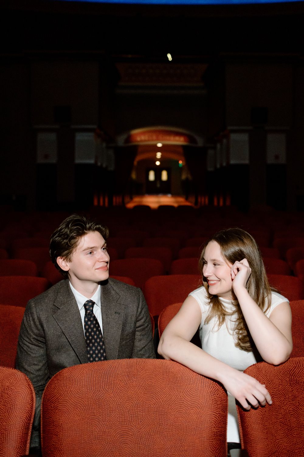 Young couple sharing a smile in a classic theater with red seats during engagement photos.