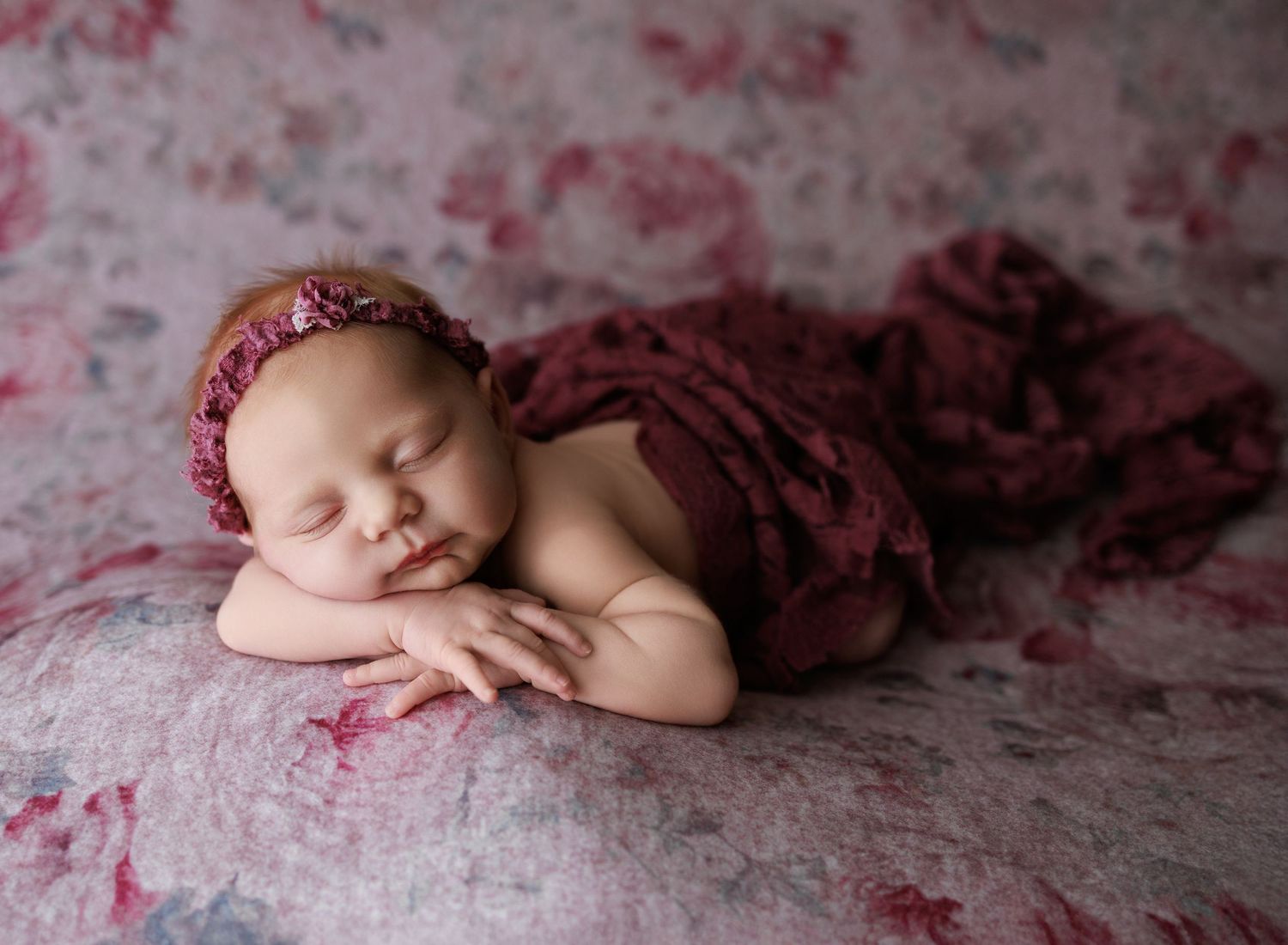 Newborn baby girl photographed in burgundy and pink tones