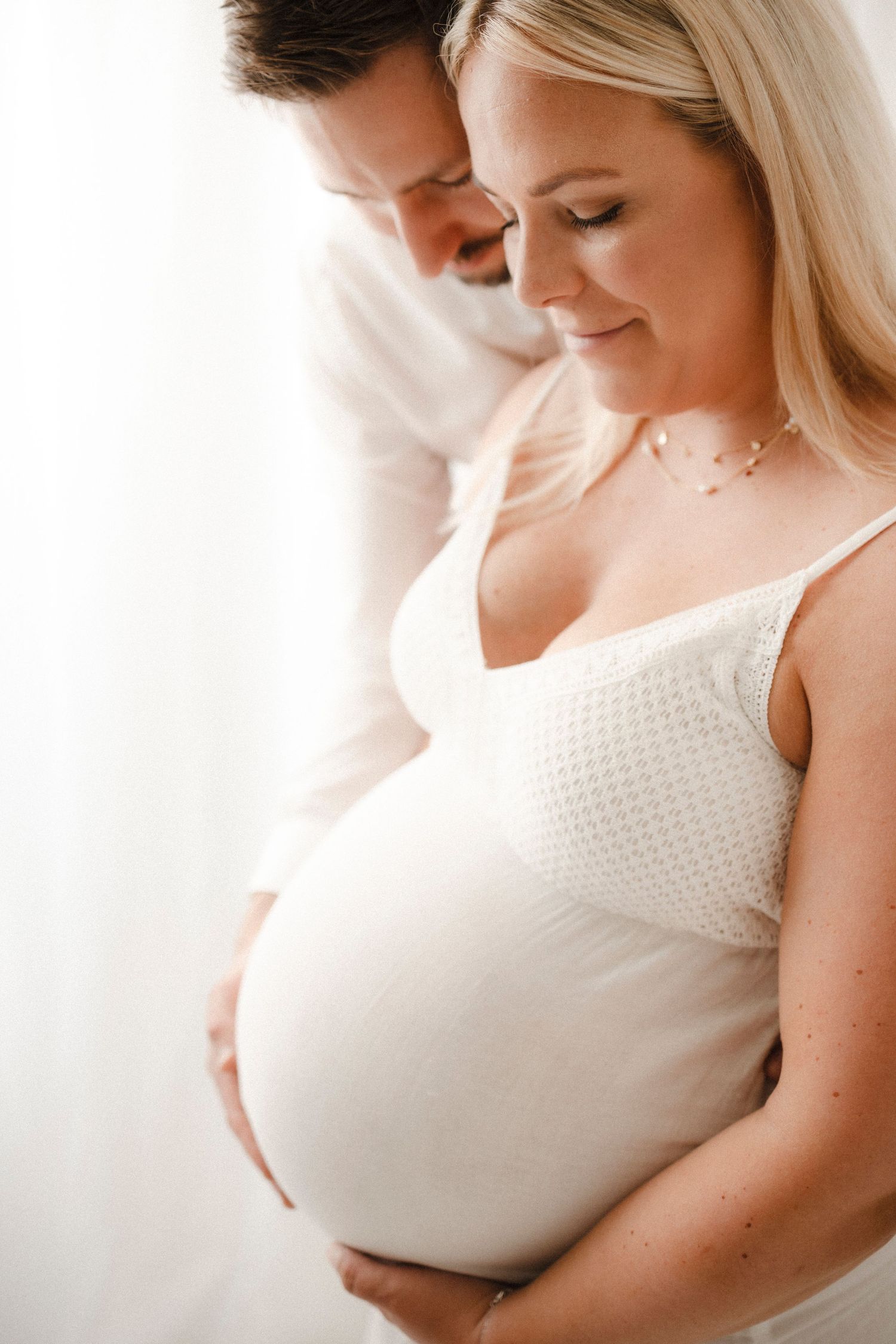 A series of intimate maternity portraits showing a woman in white against a light background in various poses.