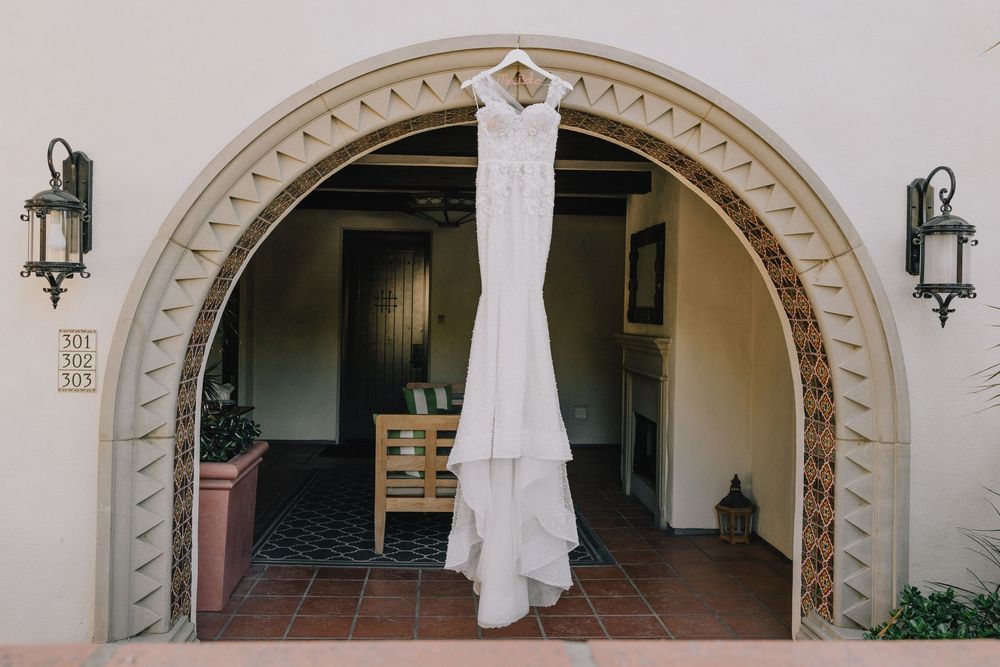 Elegant white wedding gown hangs in a Spanish-style arched doorway with terracotta tile flooring.