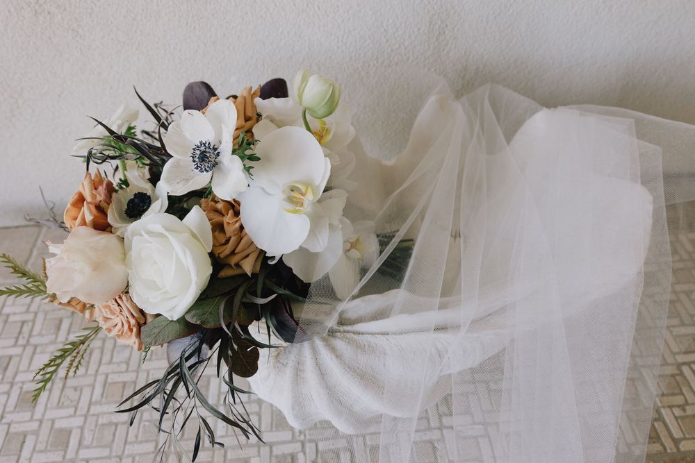 Elegant bridal bouquet with white anemones and roses beside a flowing wedding veil.