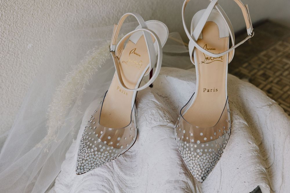 Sparkling crystal-embellished Christian Louboutin wedding heels resting on a white feathered bridal gown.