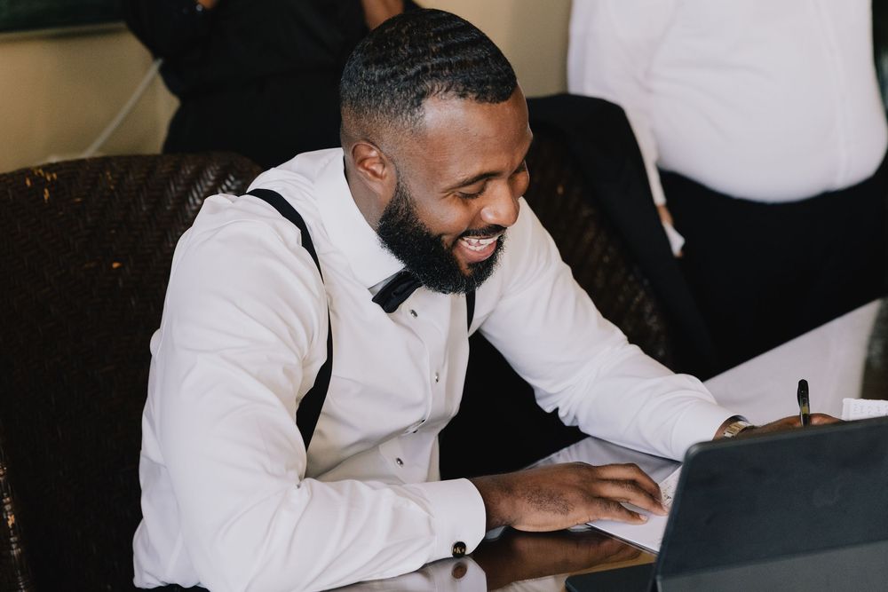 Smiling Black man in white dress shirt and bow tie reviews documents at a table during a formal event.