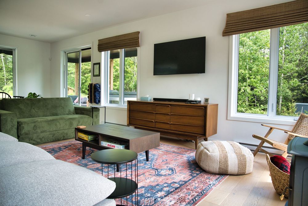 Bright living room with green sofa, wooden dresser, wall-mounted TV, and large windows.