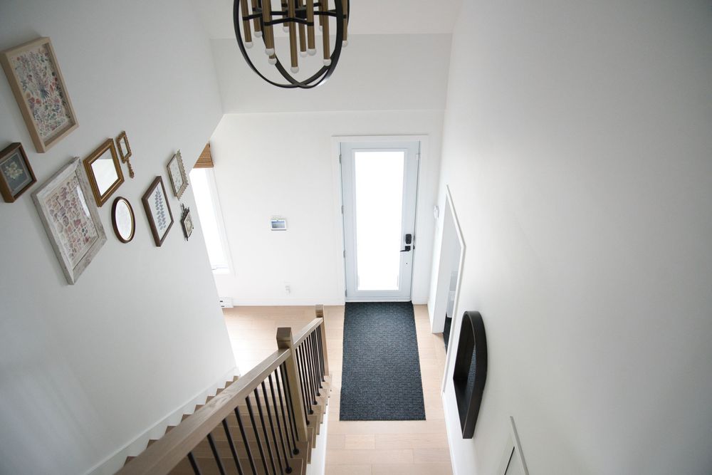 Bright white entryway with staircase, gallery wall frames, chandelier, and natural light from front door.