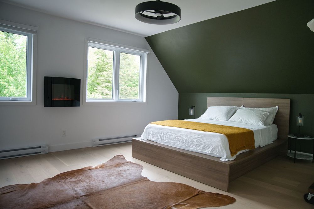 Modern bedroom with olive green accent wall, platform bed, yellow throw, and cowhide rug.