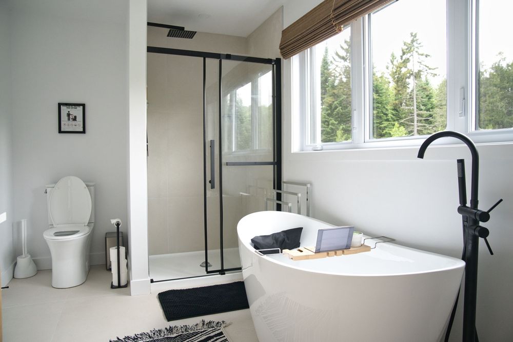 Contemporary white bathroom with freestanding soaking tub, glass shower, black fixtures, and large window.