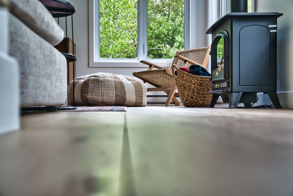 Low-angle living room view with hardwood floors, wicker basket, floor cushion, and garden window view.