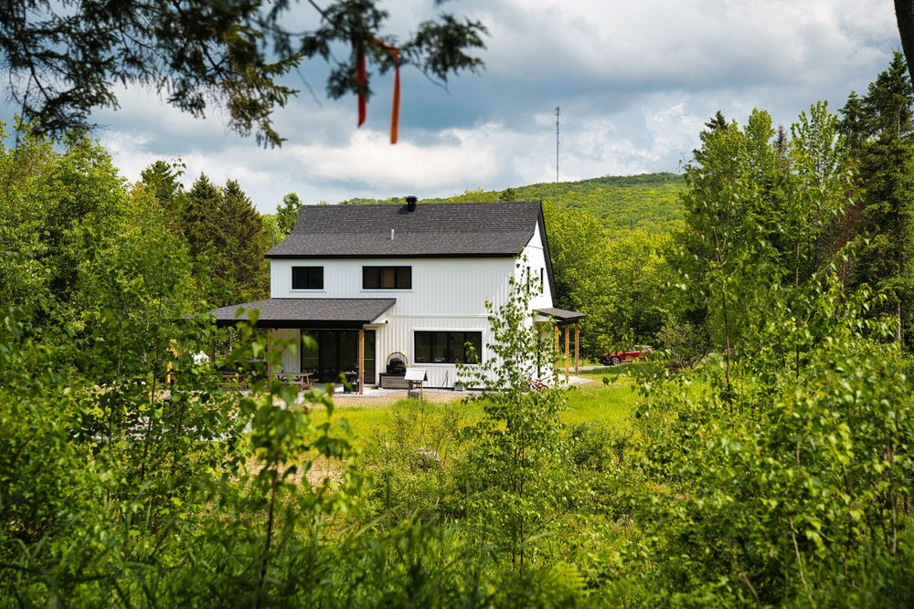 White two-story house nestled among lush green trees with mountain backdrop.