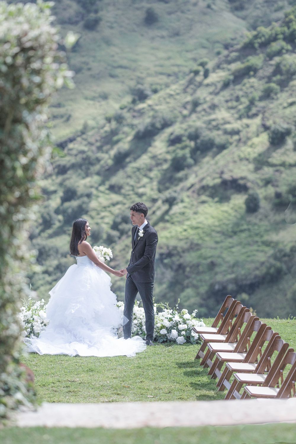 Outdoor wedding ceremony setup with wooden chairs against a backdrop of rolling green mountains.