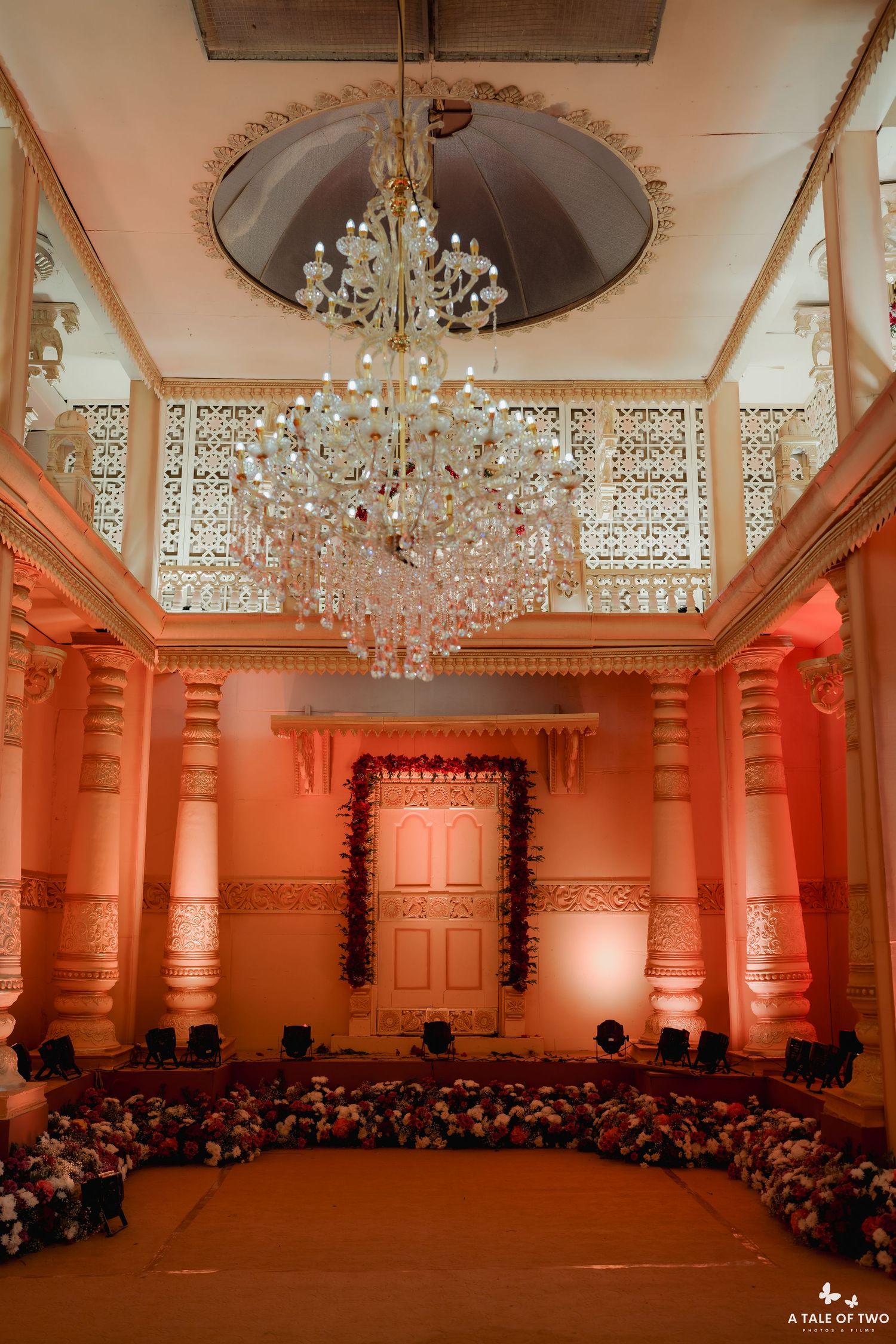 Grand Indian wedding mandap interior with crystal chandelier, pink arched columns, and floral decorations on the floor.