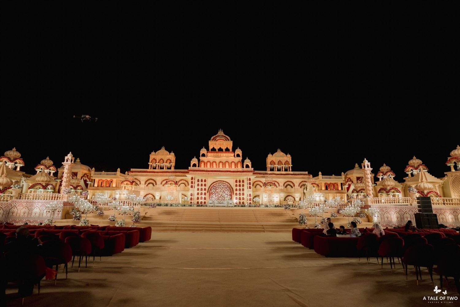 Stunning large-scale Indian wedding venue featuring palace-style illuminated facade with red seating arrangements at night.